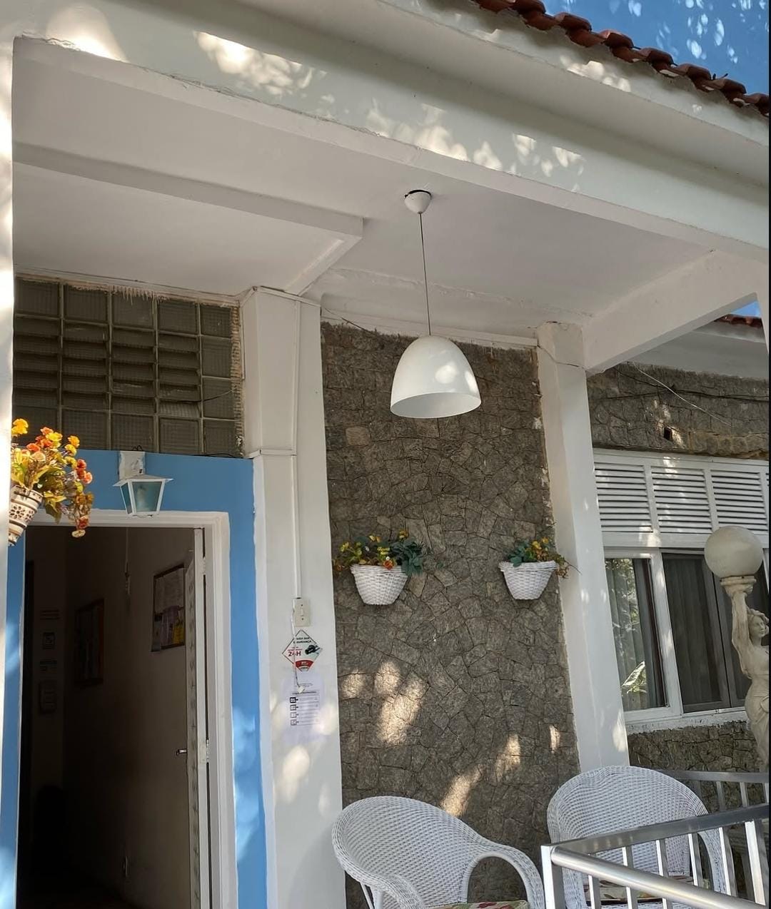Entrada da casa com canteiros de flores e poltronas